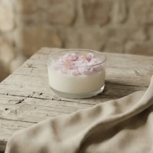 Vela artesanal de soja con flores rosas de cera en recipiente de cristal sobre mesa rústica