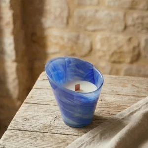 Vela de masaje profesional en recipiente de cristal azul con mecha de madera sobre mesa rústica