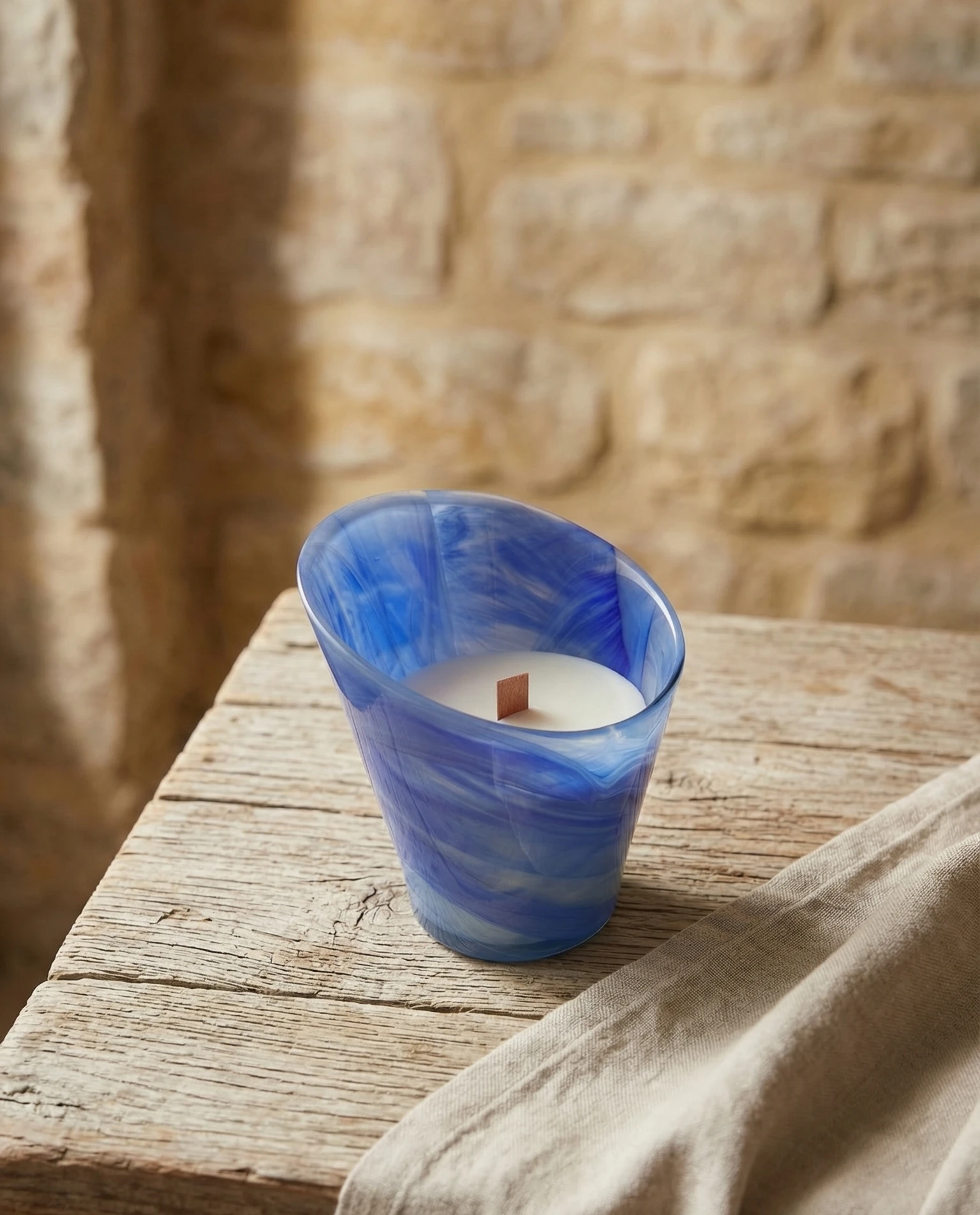 Vela de masaje profesional en recipiente de cristal azul con mecha de madera sobre mesa rústica