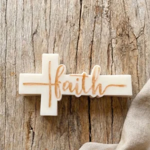 Vela decorativa de soja en forma de cruz con palabra Faith sobre mesa de madera rústica