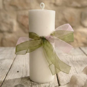 Vela de pilar blanca aroma jengibre con lazo decorativo sobre mesa rústica