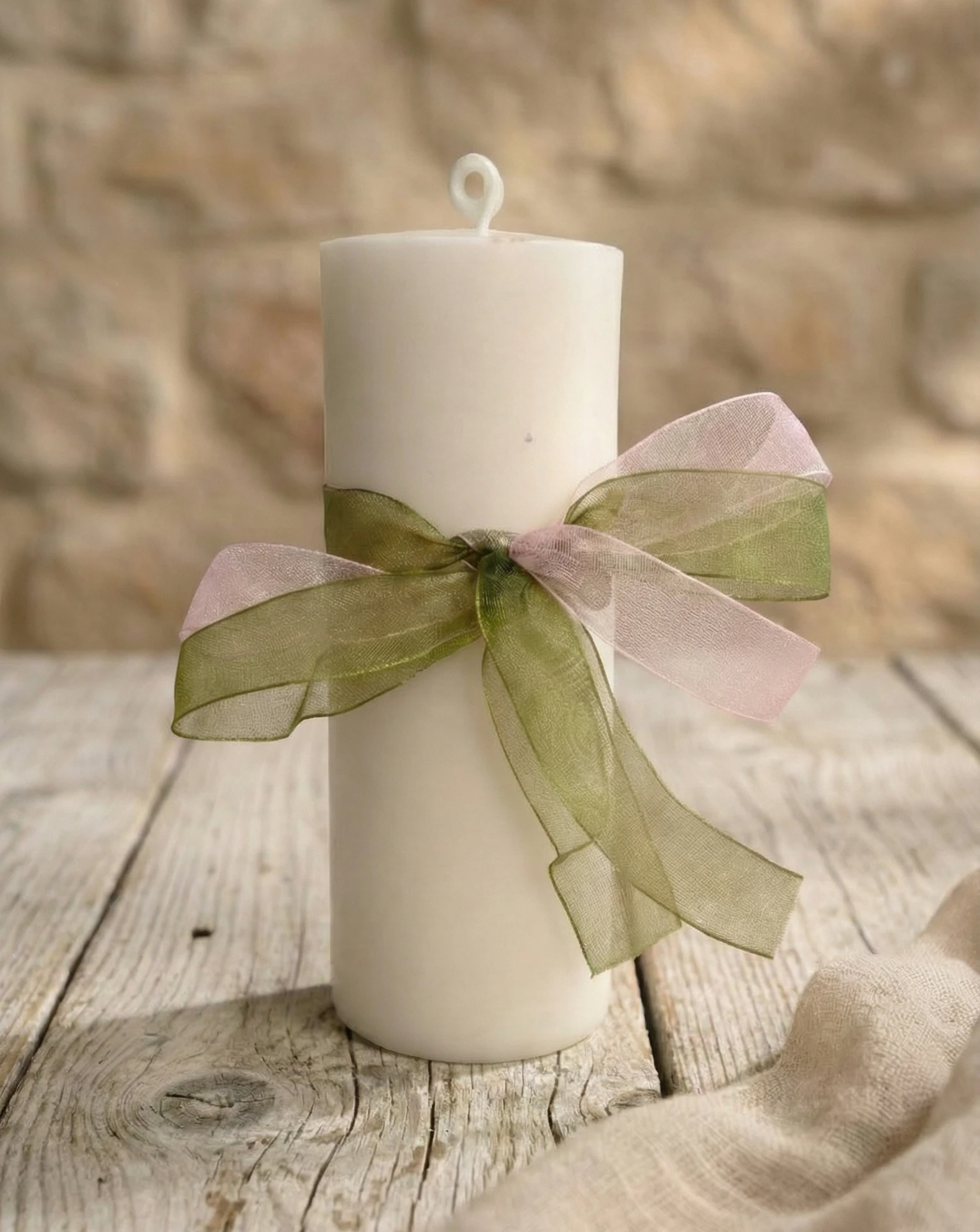 Vela de pilar blanca aroma jengibre con lazo decorativo sobre mesa rústica