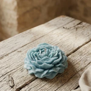 Vela decorativa artesanal de soja con forma de peonía azul turquesa sobre mesa de madera rústica