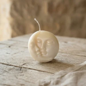 Vela artesanal de soja con rostro de luna sobre mesa de madera rústica