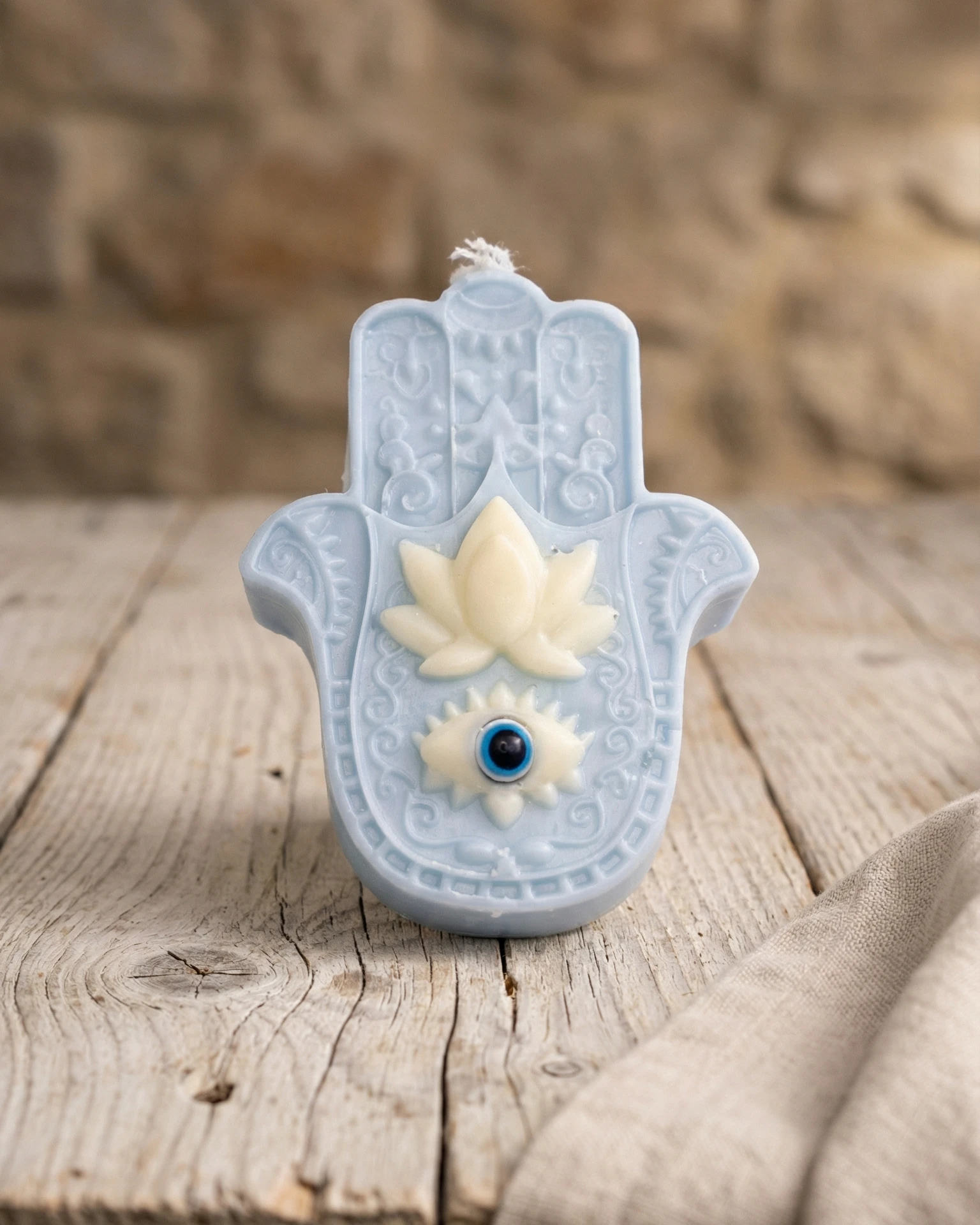 Vela Mano de Fátima azul de soja con ojo protector sobre mesa de madera rústica