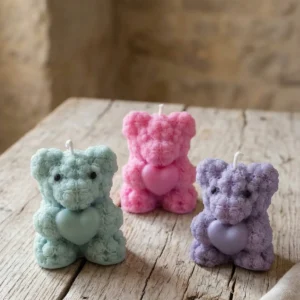 Velas de soja decorativas artesanales con forma de osito con corazón en colores pastel sobre mesa de madera rústica