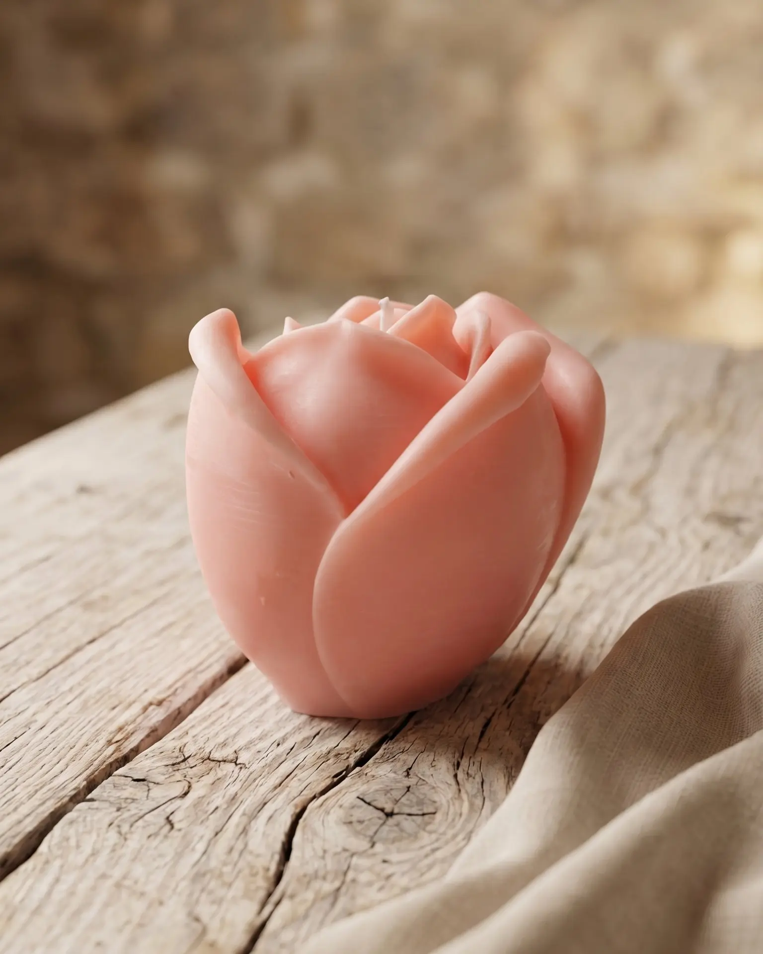 vela rosa pastel en forma de rosa sobre mesa de madera con tela neutra