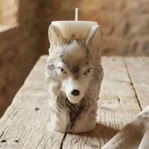 Vela decorativa tipo pilar con cara frontal de lobo blanco sobre mesa de madera envejecida